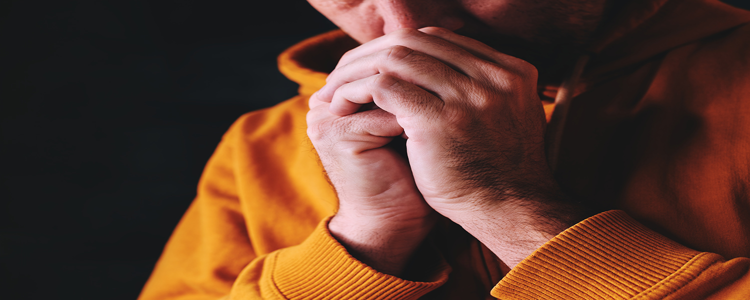 Christian man praying to God in dark room with clasped hands, close up with selective focus